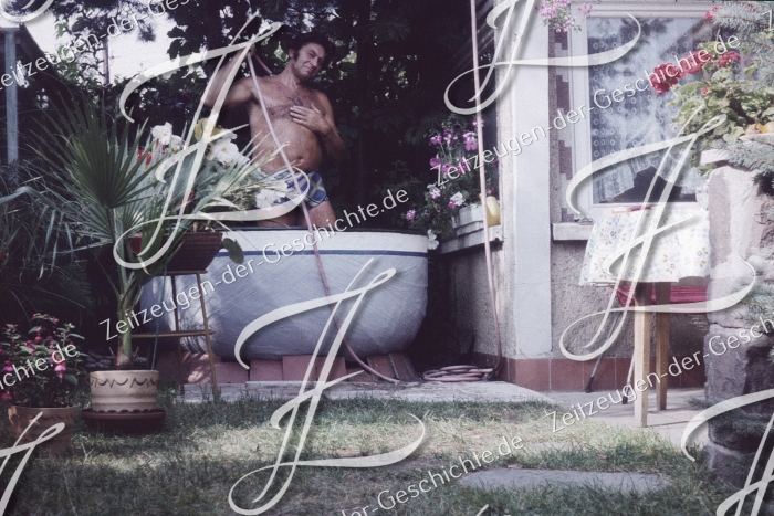 Mann duscht im Garten mit Gartenschlauch, 1975